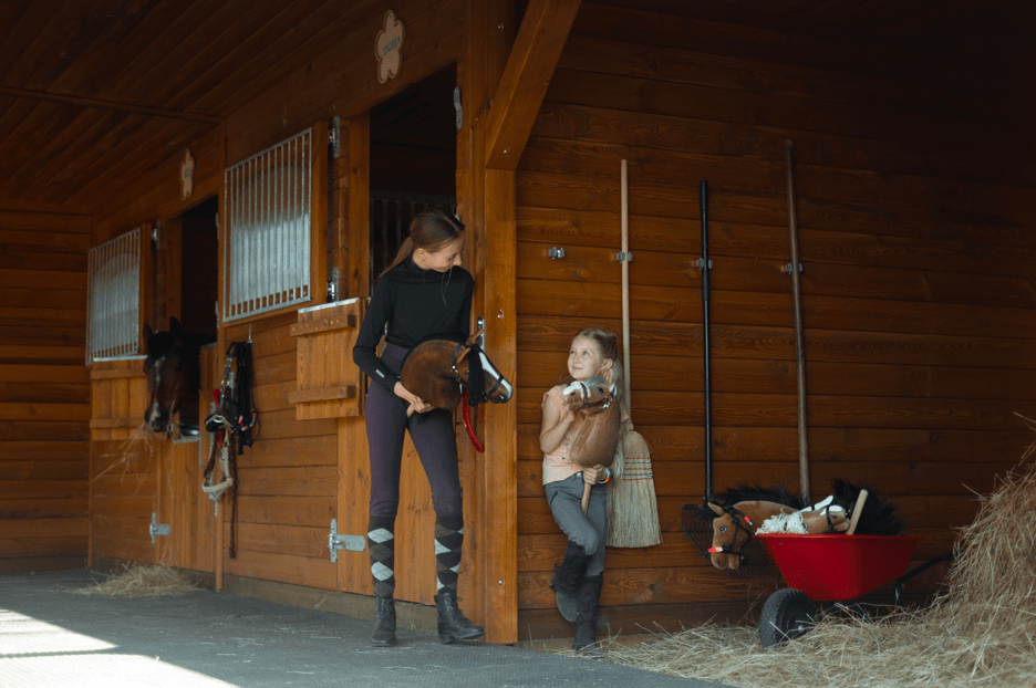 Ungdomar med käpphästar utanför ridklubbens stall i trä