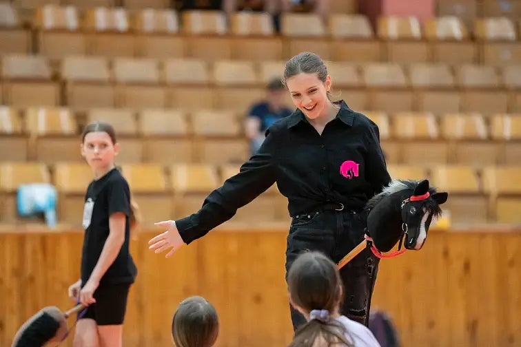 Uppvisning i Hobby Horsing i en idrottshall, med en kvinna som håller en svart käpphäst