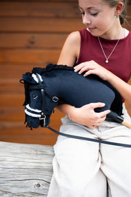 Girl in a burgundy top holds Hobby Horse Mahal with Black Halter in her arms, here in a black bridle with white fur