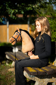 Girl in a black jumper on a park bench in the evening sun holding Hobby Horse Samantha in a black bridle with reins
