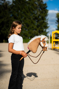 Flicka i vit topp på en sandbana med Hobby Horse Star, här i brun grimma med krämvit päls och bruna tyglar av rep
