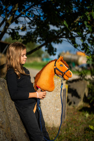 Flicka i svart tröja som lutar sig mot ett stenblock under ett träd och håller Hobby Horse Wendy i ett marinblått grimskaft
