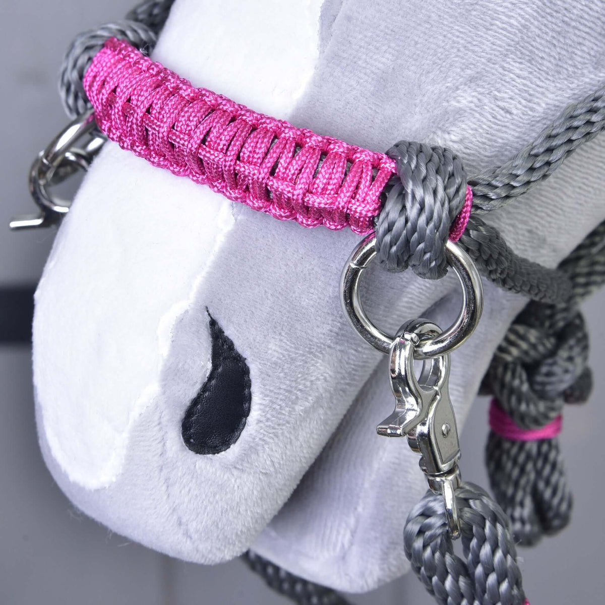 Närbild på den rosa lindade nosremmen med silverfärgad ring och karbinhake på den grå repgrimman på en käpphäst