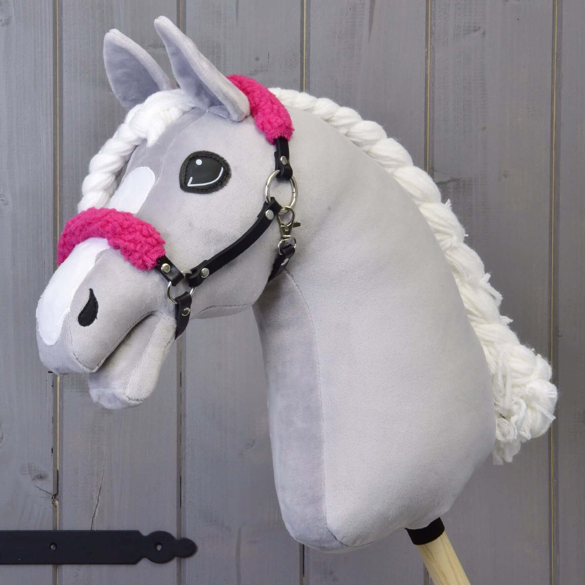 A grey plush Hobby Horse with a white blaze and braided mane wears the black halter with curly bright pink fur