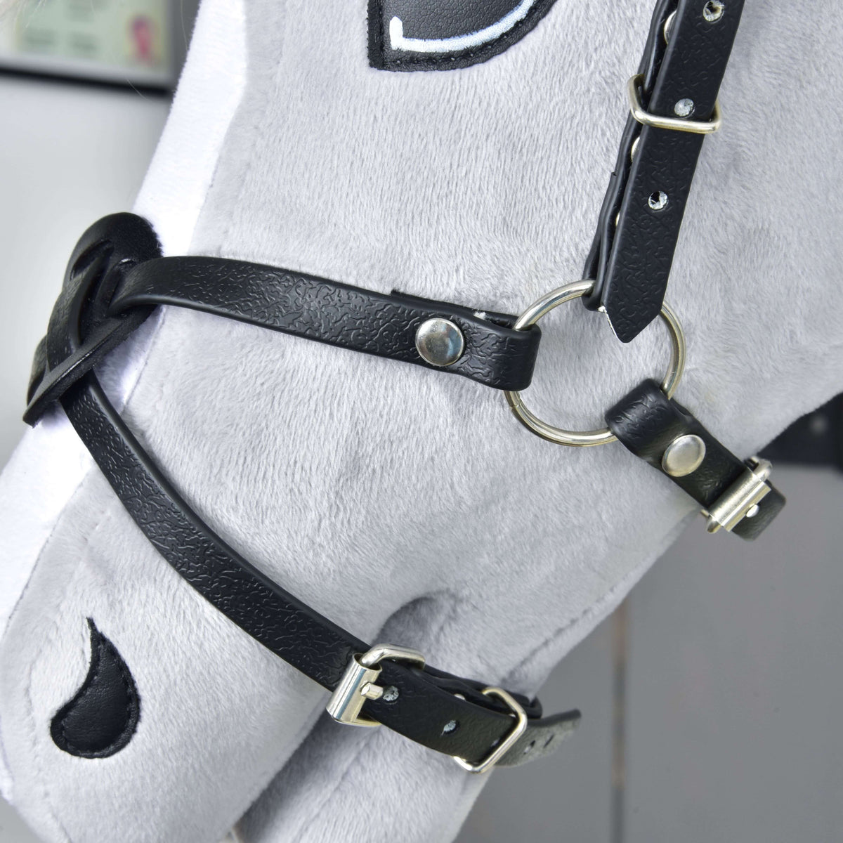 Side view of the Noseband Mexico Black on a grey Hobby Horse: leatherette straps with silver buckles and a ring