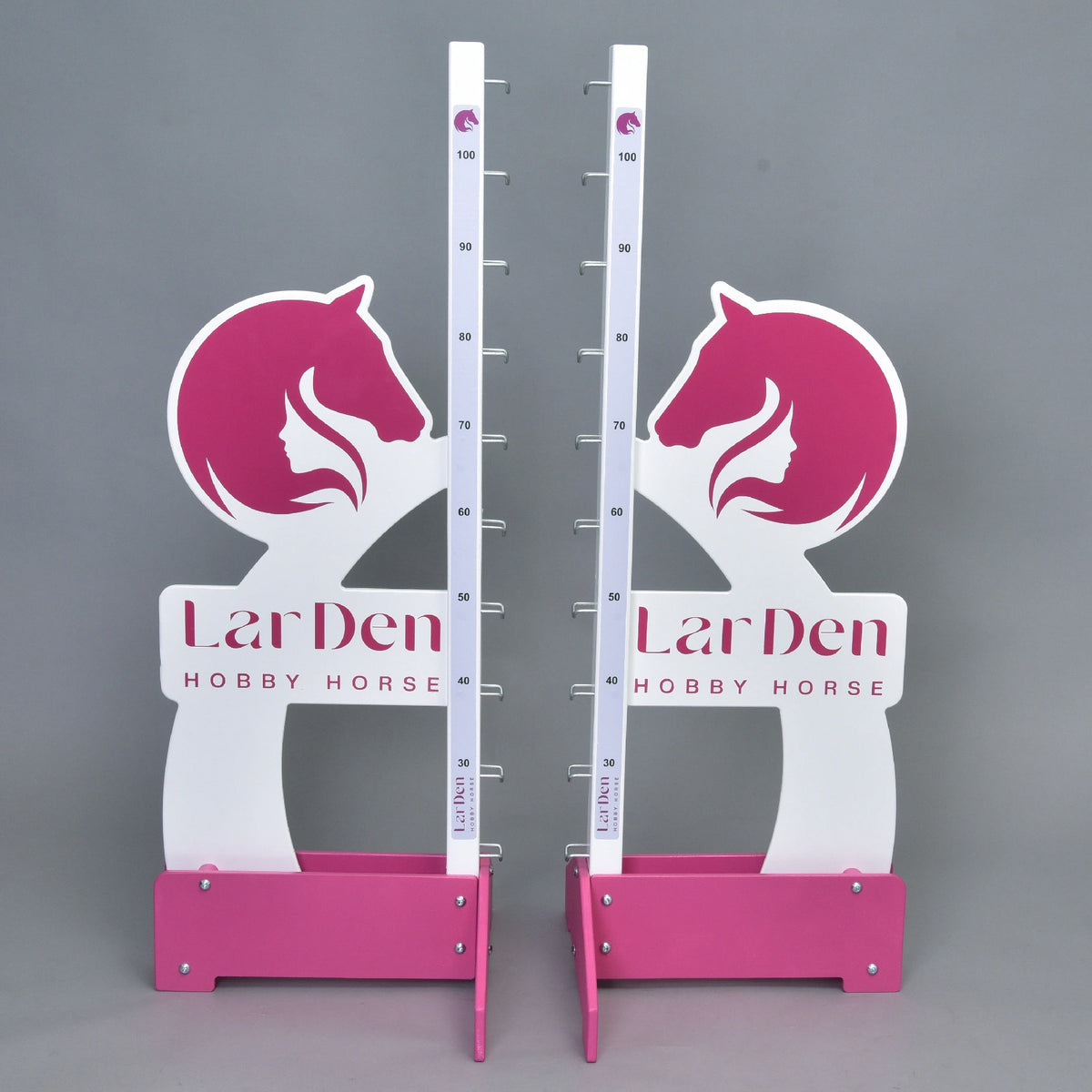 De två hinderstöden framifrån, spegelvända vingar med den rosa logotypen och en höjdskala från 30 till 100 cm