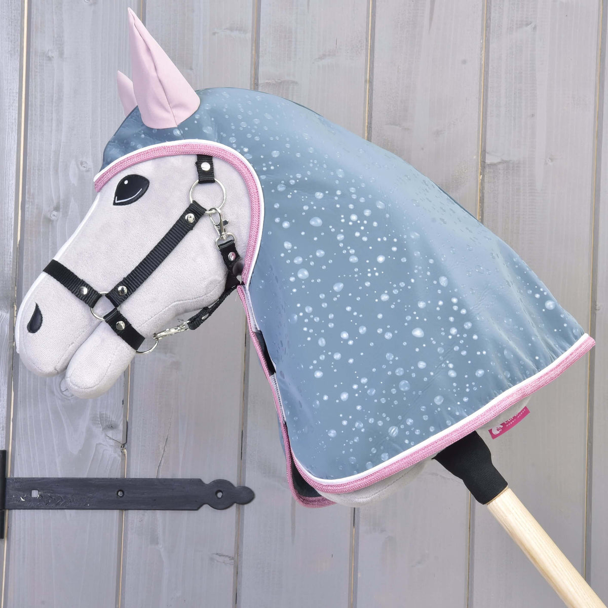Light grey Hobby Horse with a black halter wearing the grey-blue raincoat with a hood, pink ears and pink trim