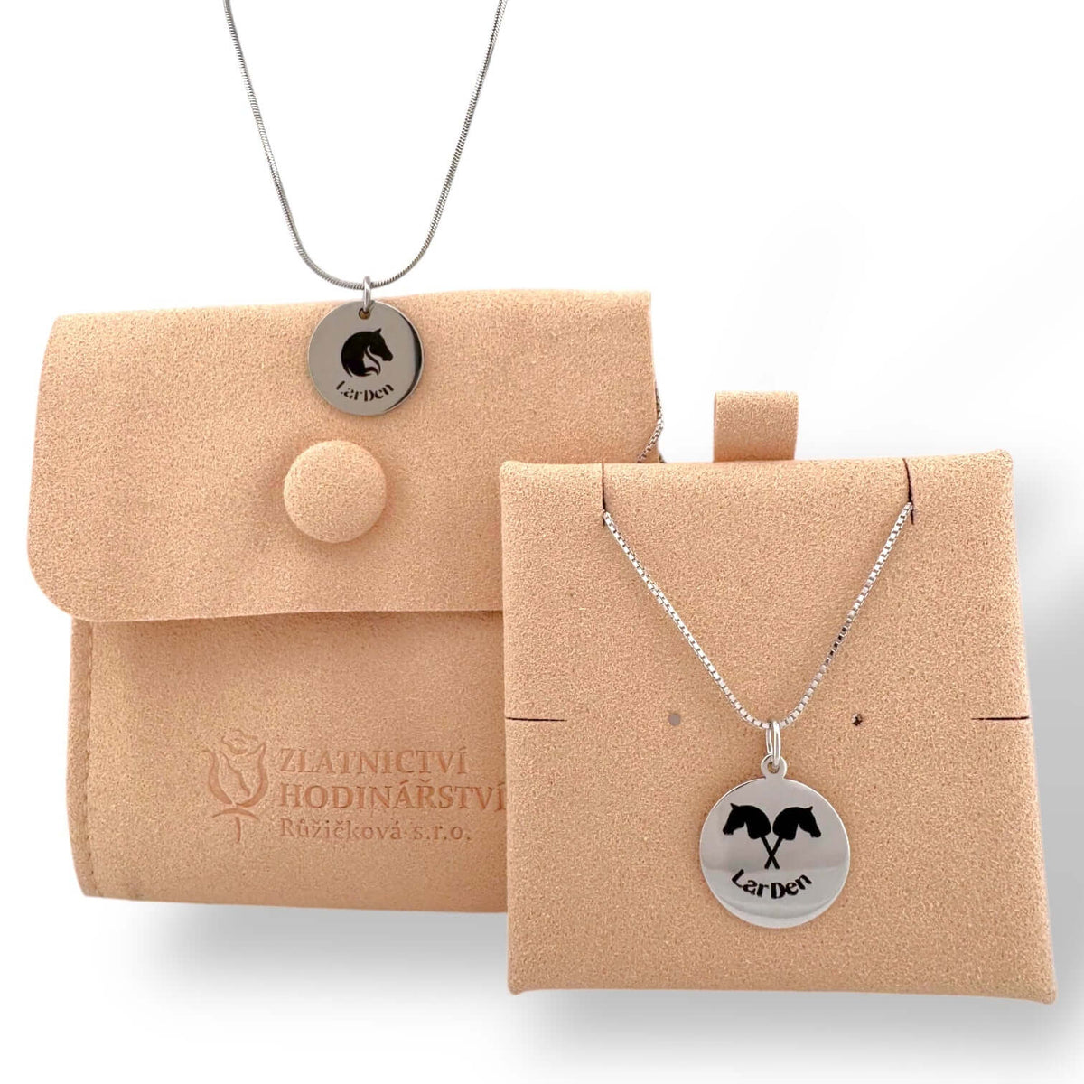 LarDen logo pendant on a snake chain over a peach suede pouch, next to a crossed horse heads pendant on a card
