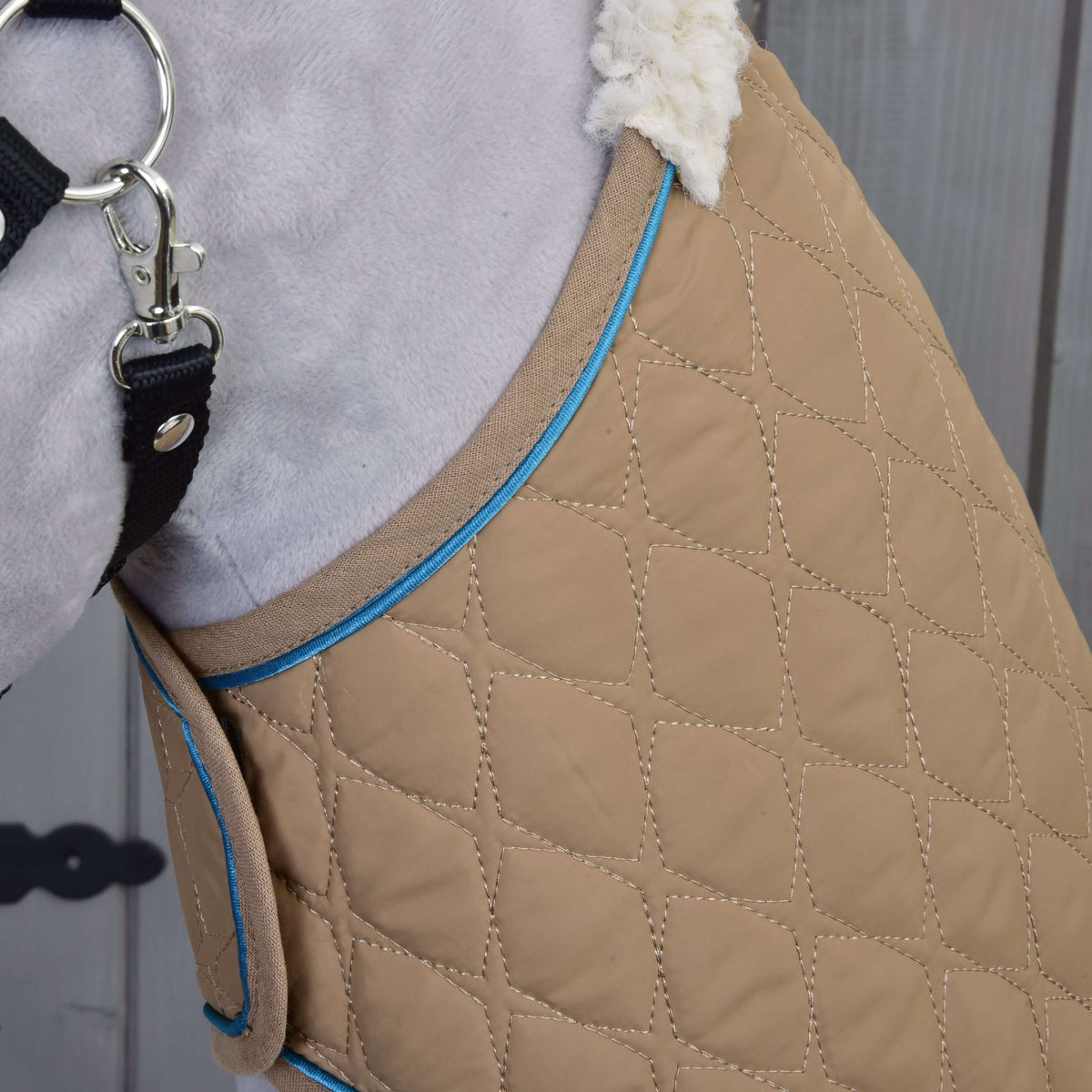 Närbild på det beige rombquiltade täcket med blå passpoal och krämvit sherpakrage vid en grå plyschhals