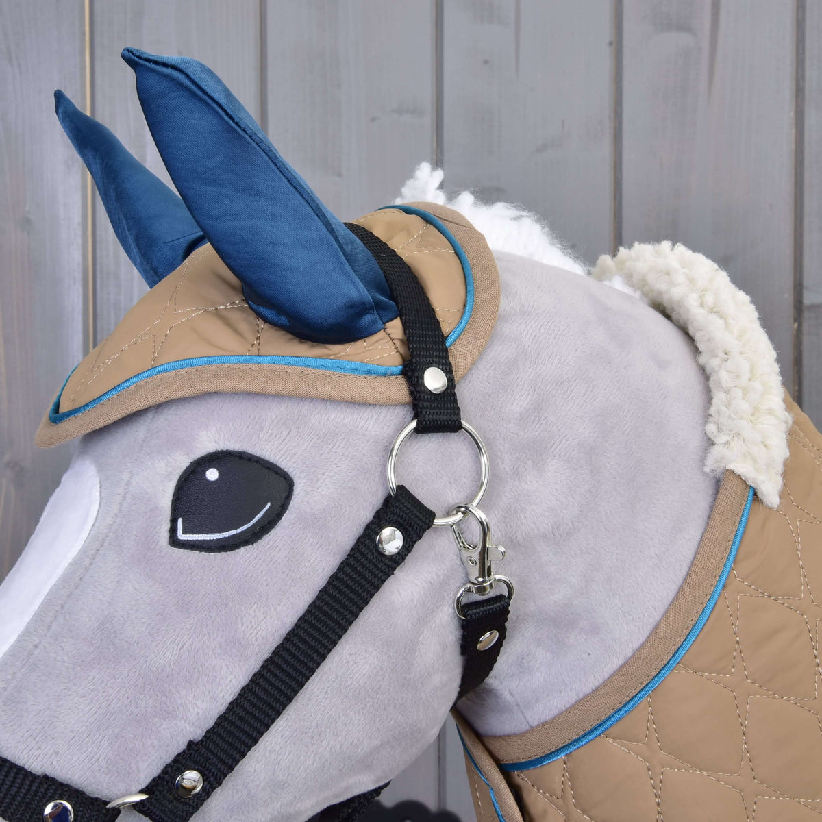 Huvudet på en grå käpphäst i närbild med flughuvan Almond Star, svart grimma och täckets fluffiga sherpakrage