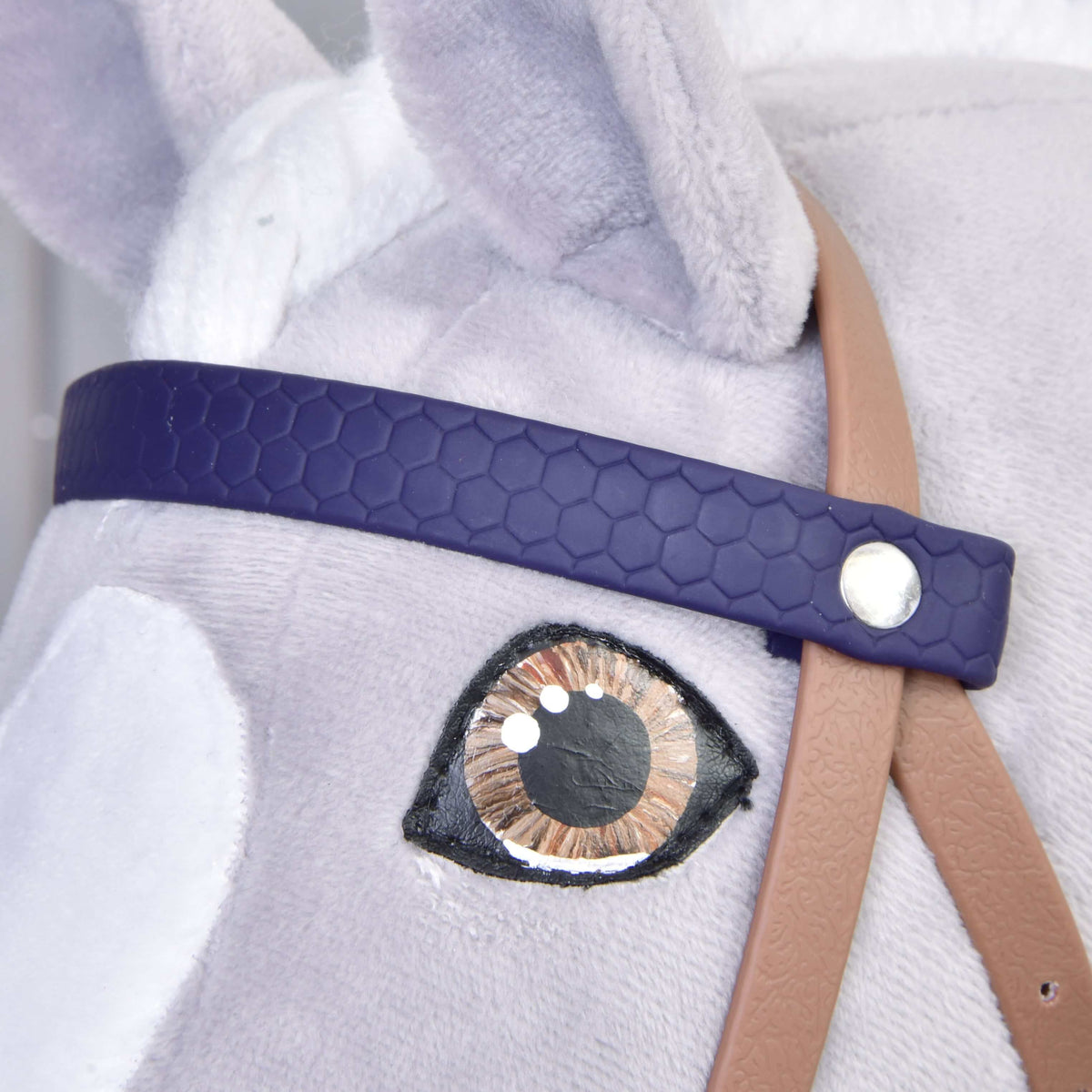 Close-up of the dark purple honeycomb browband with silver rivet above the brown eye of a grey Hobby Horse