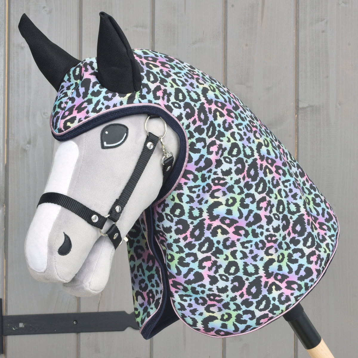 Light grey Hobby Horse in a black halter wearing the Raincoat Confetti, pastel leopard print covering head and neck
