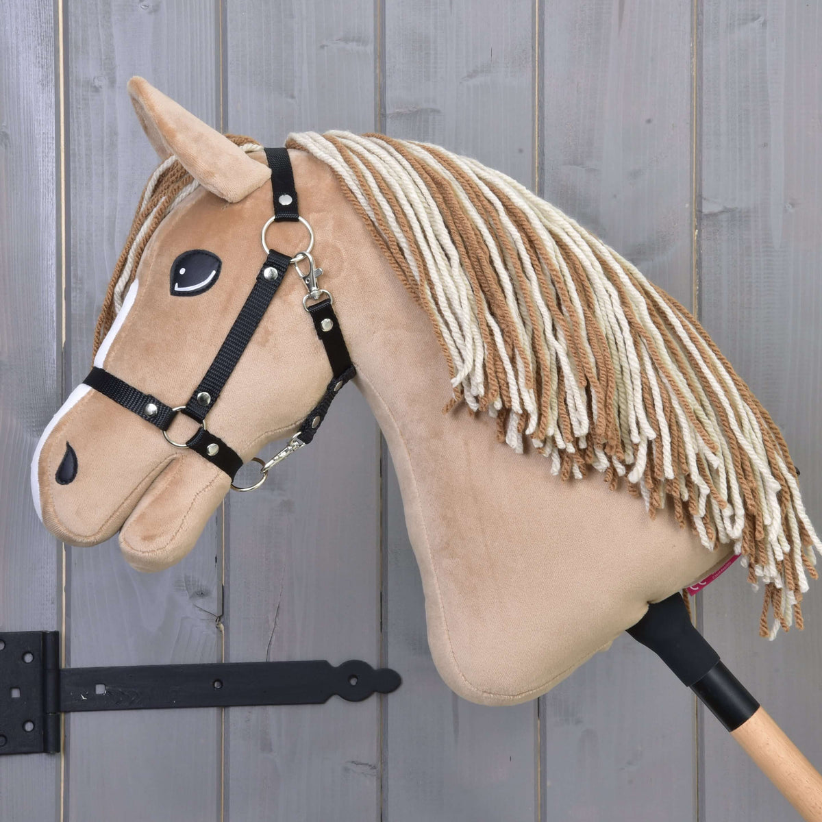 Hobby Horse Bren med svart grimma från sidan, sänkt huvud, lång man av brunt och krämfärgat garn över den ljusbruna halsen