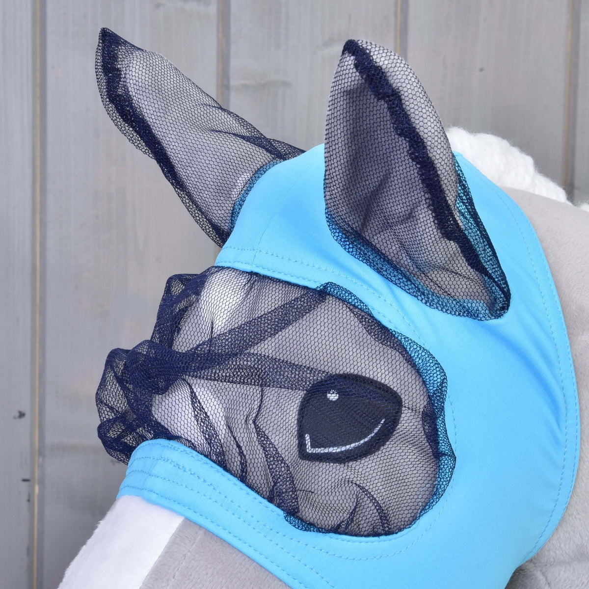 Närbild av Hobby Horse flugmask på ett grått käpphästhuvud: öron av marinblått nät och ögonnät insydda i ljusblått tyg