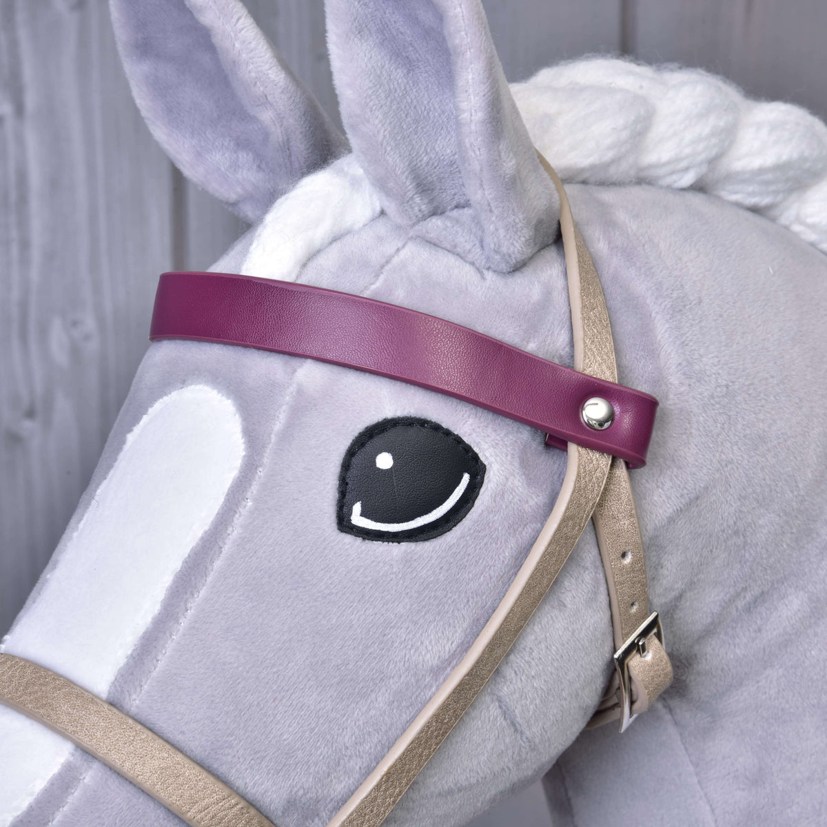 Close-up of the bordeaux browband with a silver rivet and the beige cheek strap with buckle on a grey Hobby Horse