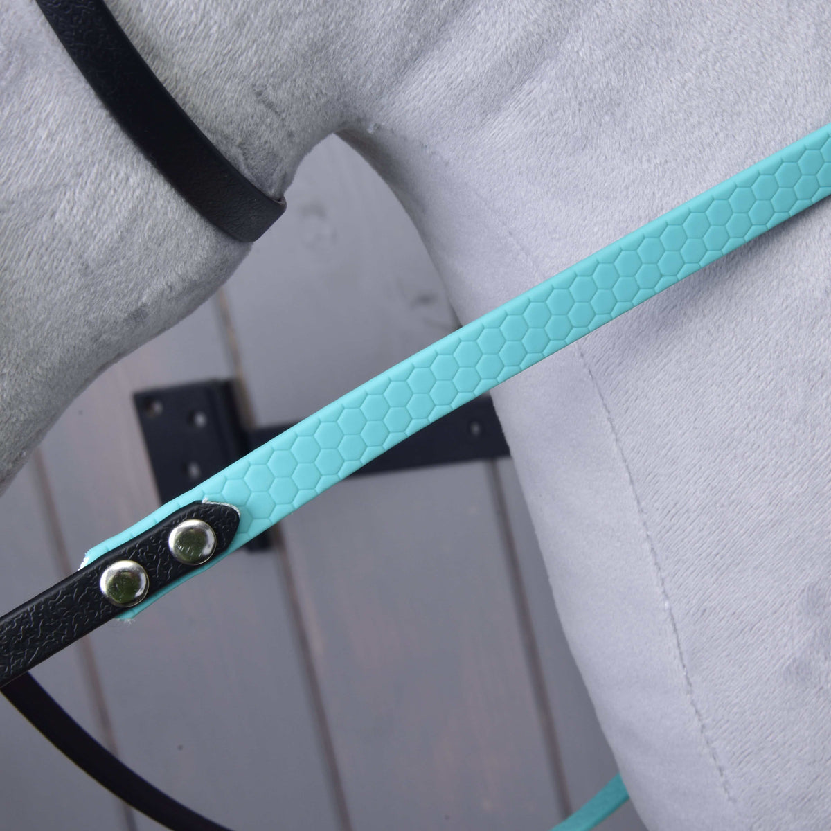 Close-up of the turquoise honeycomb-textured rein riveted to a black strap against grey plush