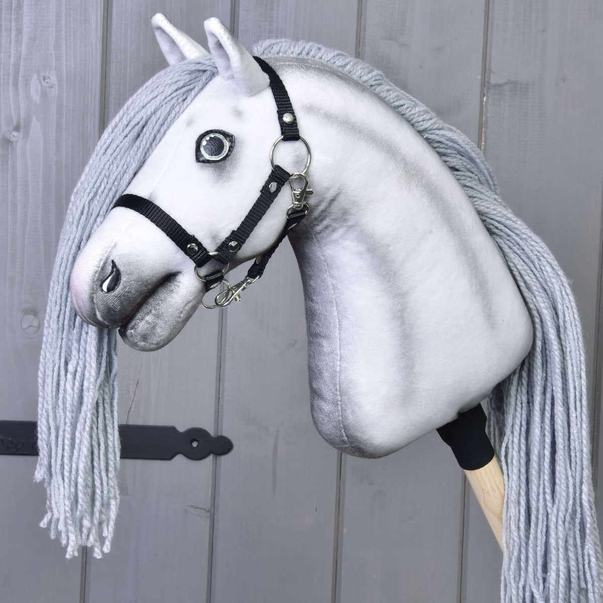 Hobby Horse enhörning Silver utan horn, i svart grimma, på en träkäpp mot grå brädor