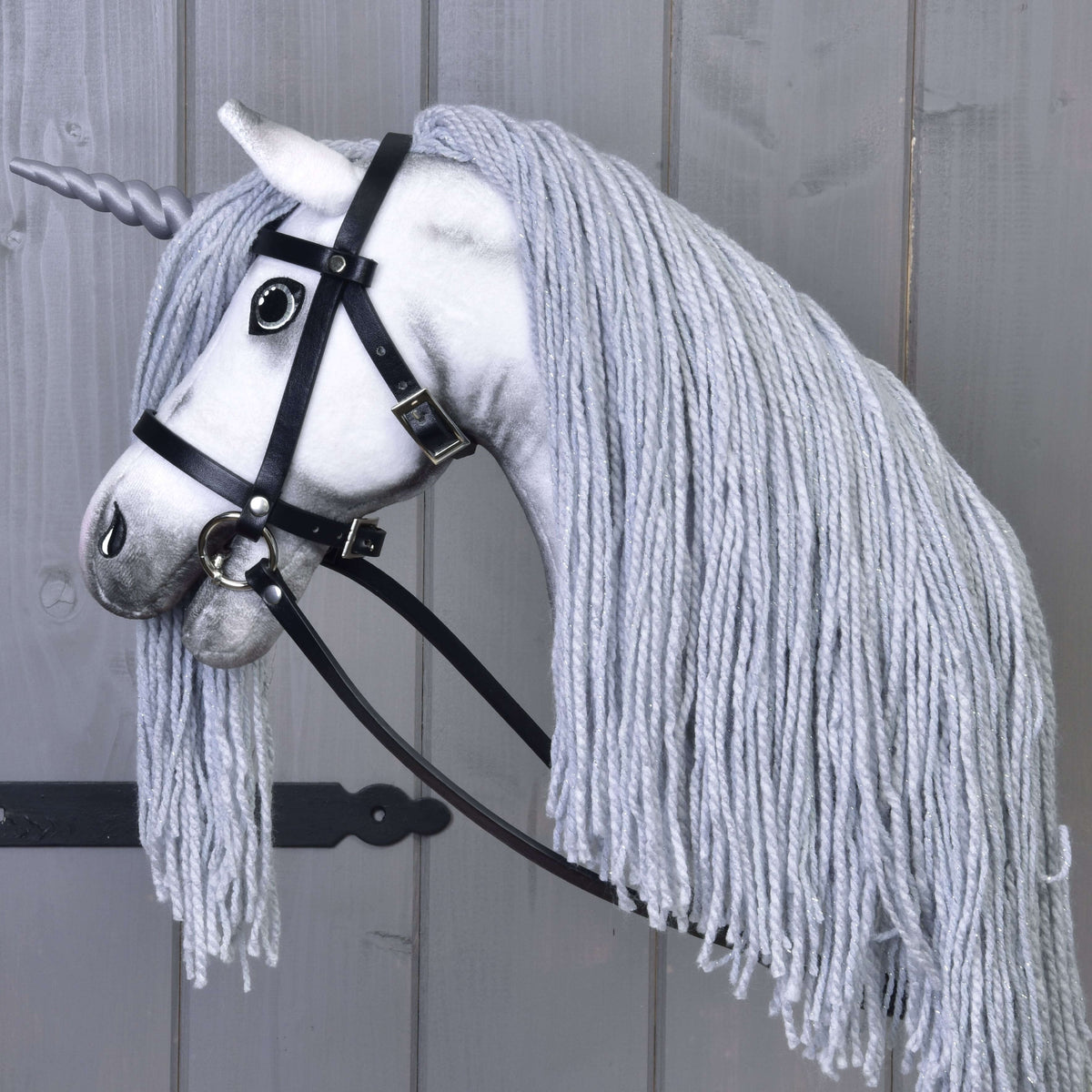 Hobby Horse enhörning Silver från sidan i sitt svarta träns med tyglar, den långa grå manen av garn faller över halsen