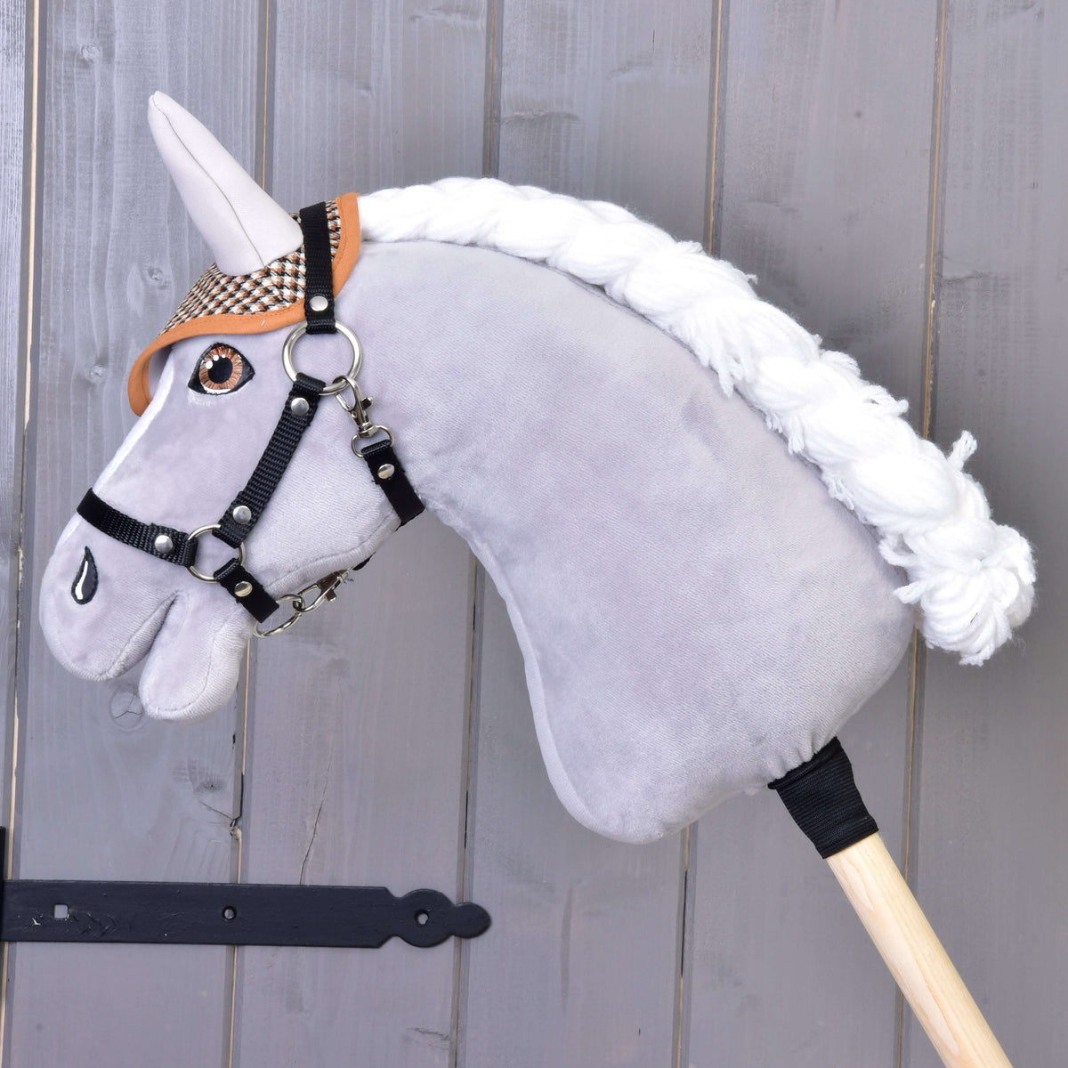 A grey plush Hobby Horse with a white braided mane and black halter wears the brown houndstooth ear bonnet