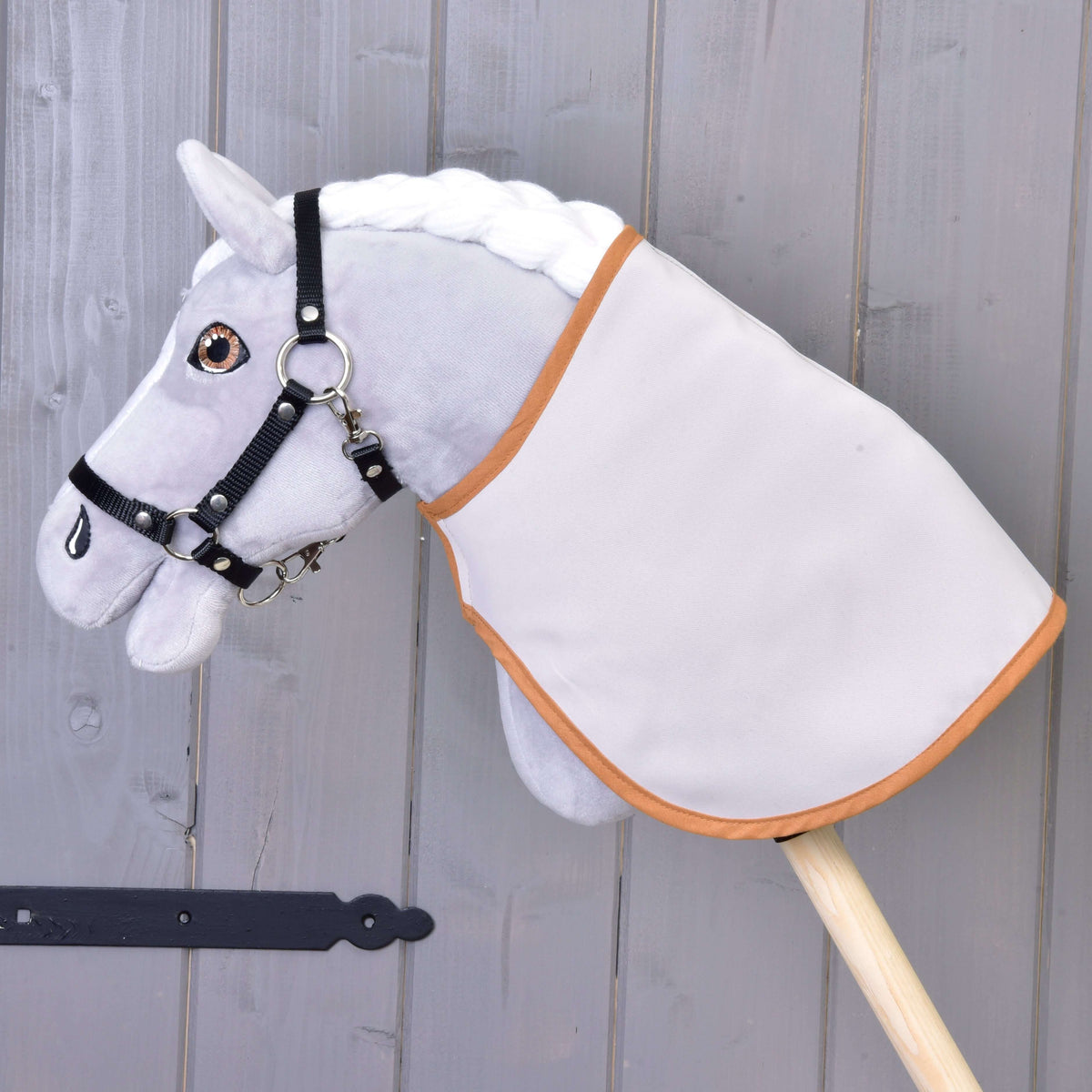 A grey plush Hobby Horse in a black halter wears the blanket turned to its plain light side with caramel trim