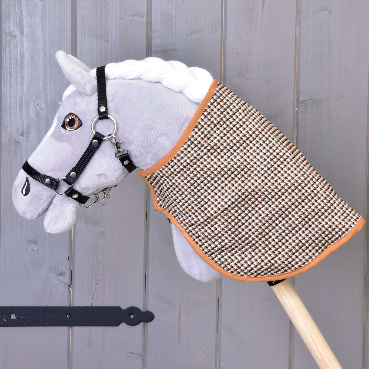 A grey plush Hobby Horse in a black halter wears the blanket with its brown houndstooth side out by a grey wall