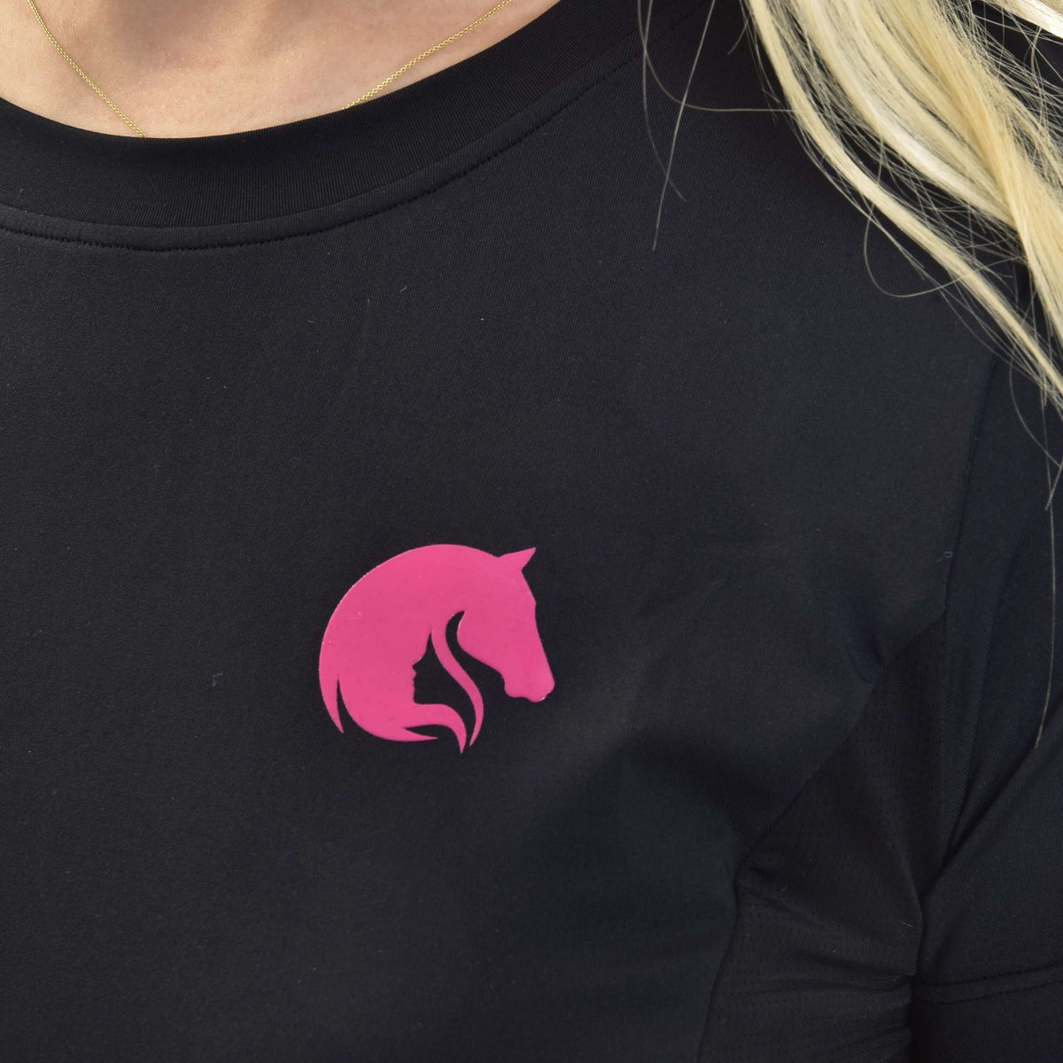 Närbild av den rosa hästhuvudsloggan på en svart sporttröja med rund hals, buren med ett tunt guldhalsband