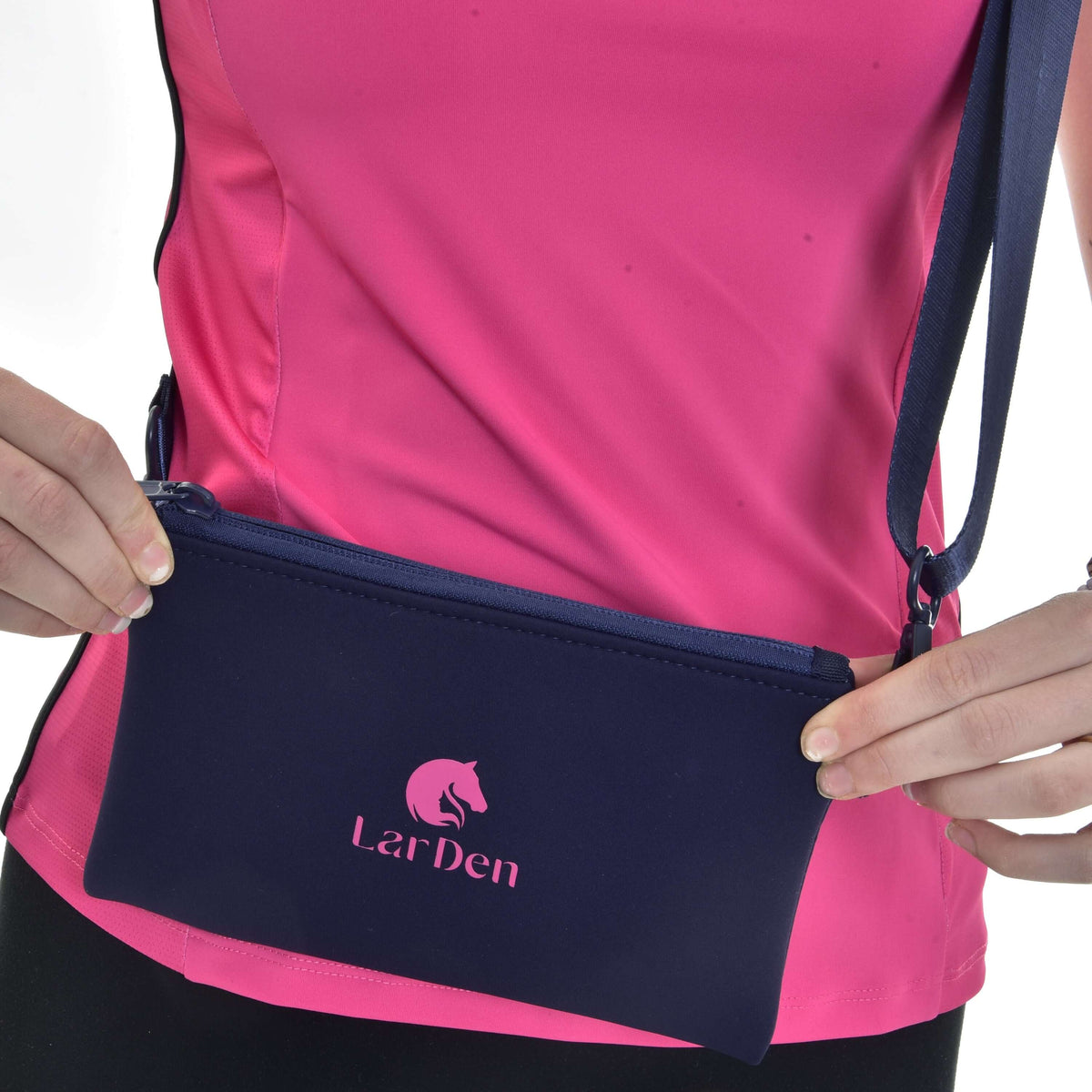 Close-up of hands holding the Hobby Horse Cross body bag at the hip, pink LarDen logo on navy neoprene