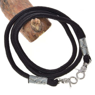 LarDen Hobby Horse Reins Black, braided black cord with silver-grey wraps and two silver snap hooks, coiled on a wooden log
