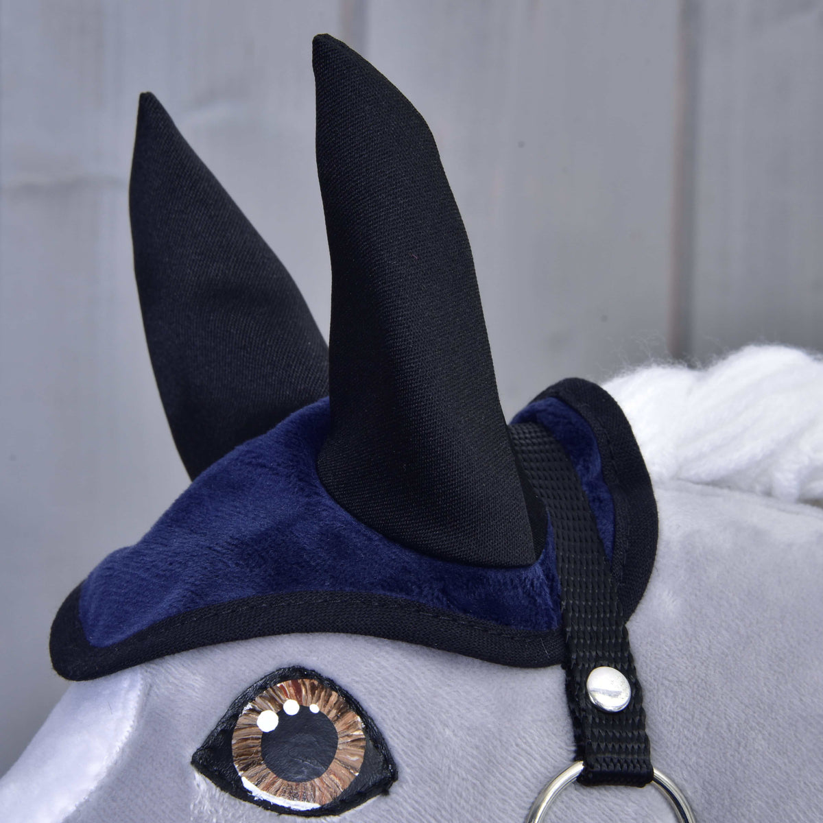 Close-up of the dark blue velvety ear bonnet with tall black ears and black binding above a brown eye