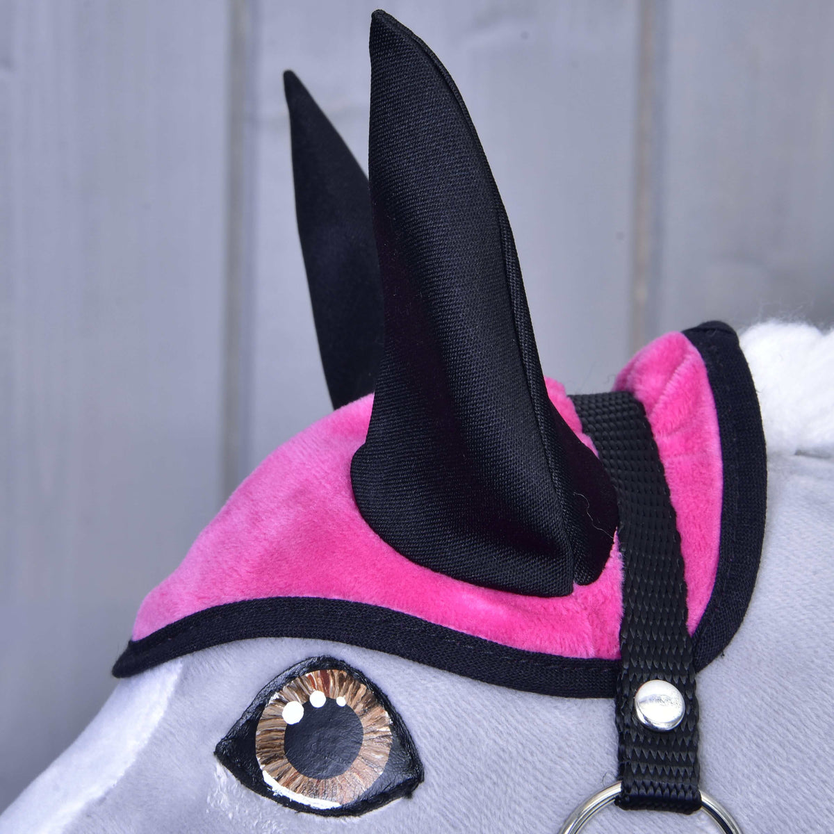 Close-up of the hot pink velvety ear bonnet with black ears and black binding above a brown eye