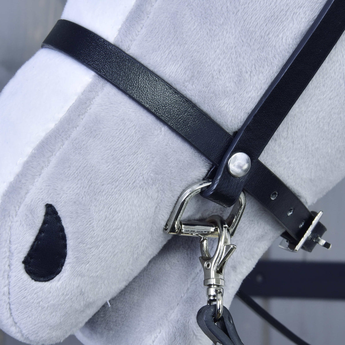 Detail of the black leatherette noseband with silver D-ring and the snap hook of the reins on a light grey Hobby Horse muzzle