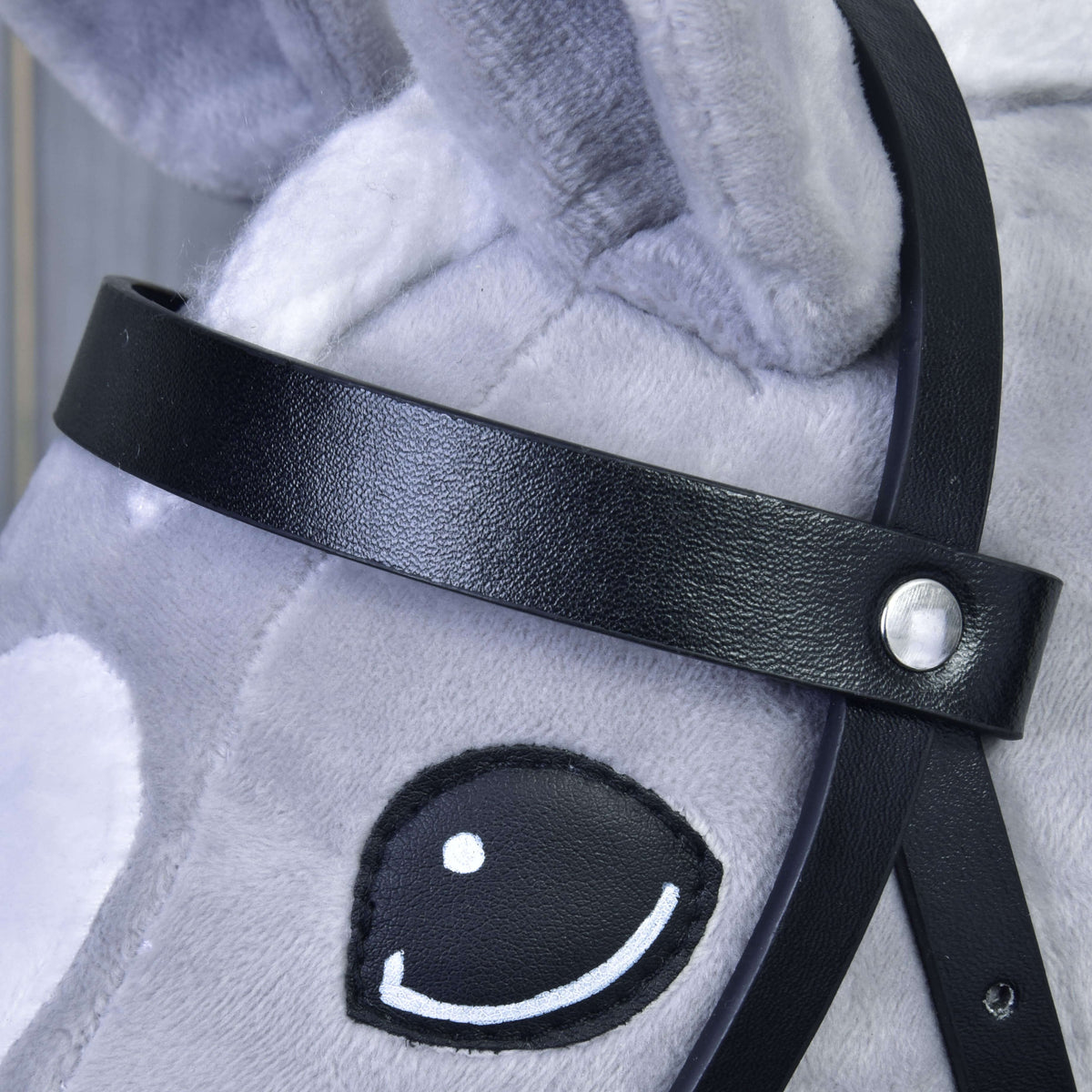 Close-up of the smooth black leatherette browband with a silver rivet above the eye of a light grey Hobby Horse