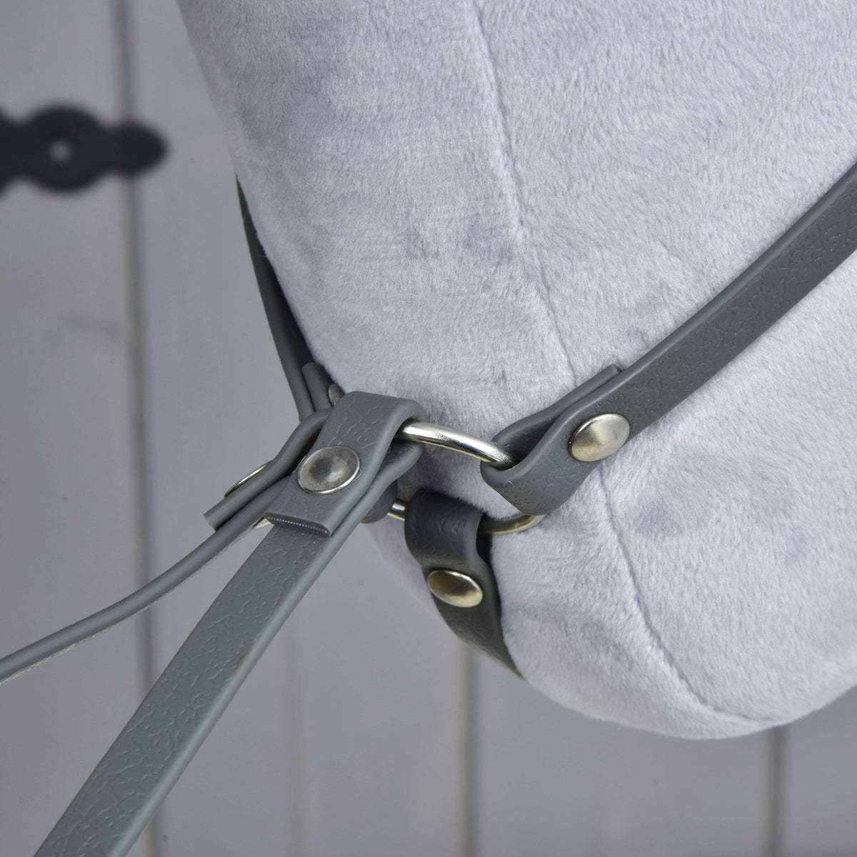 Närbild under plyschhalsen där martingalens halsrem möter gaffelremmarna vid en silverfärgad ring med nitar