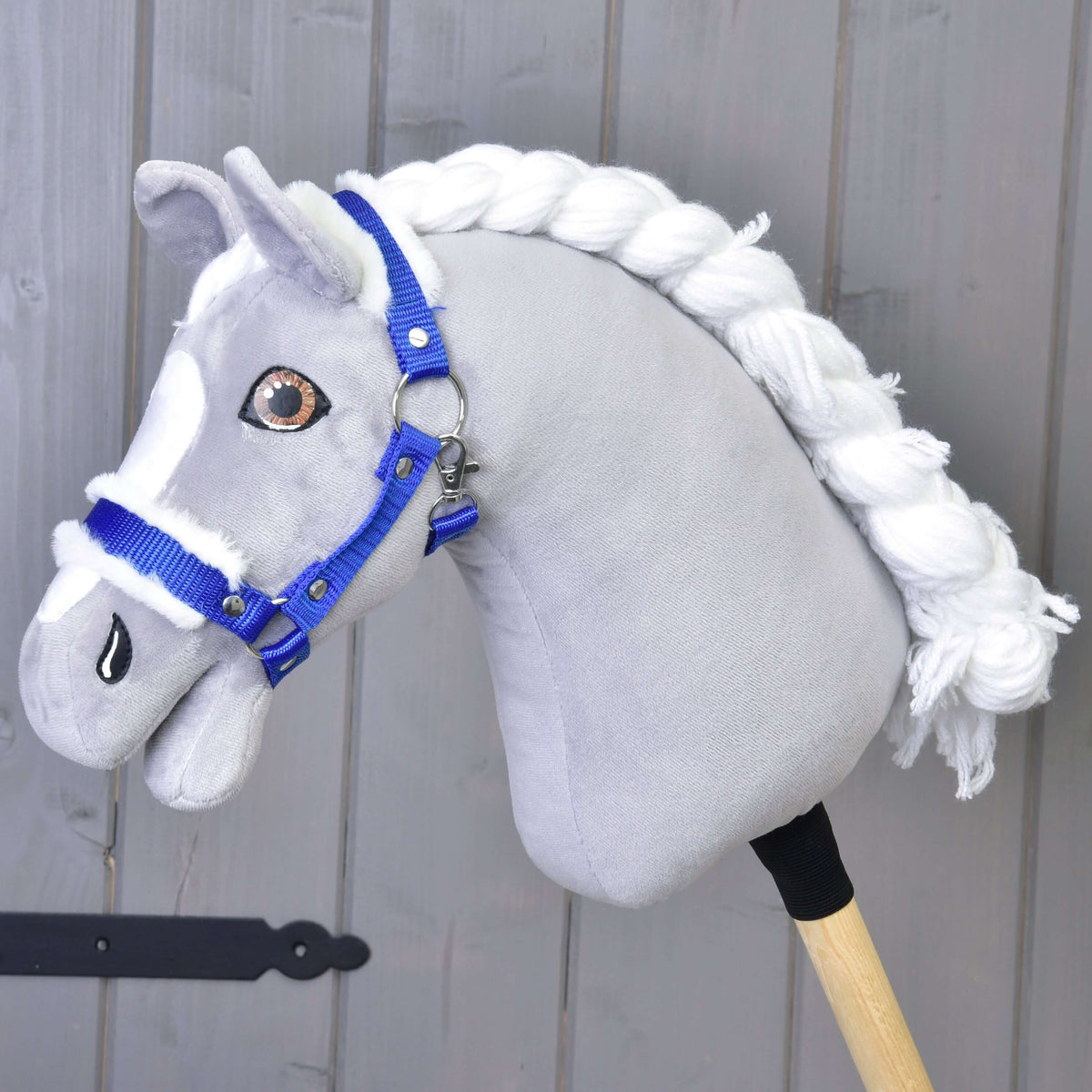 A grey plush Hobby Horse with a white braided mane and brown eyes wears the royal blue halter with white fur