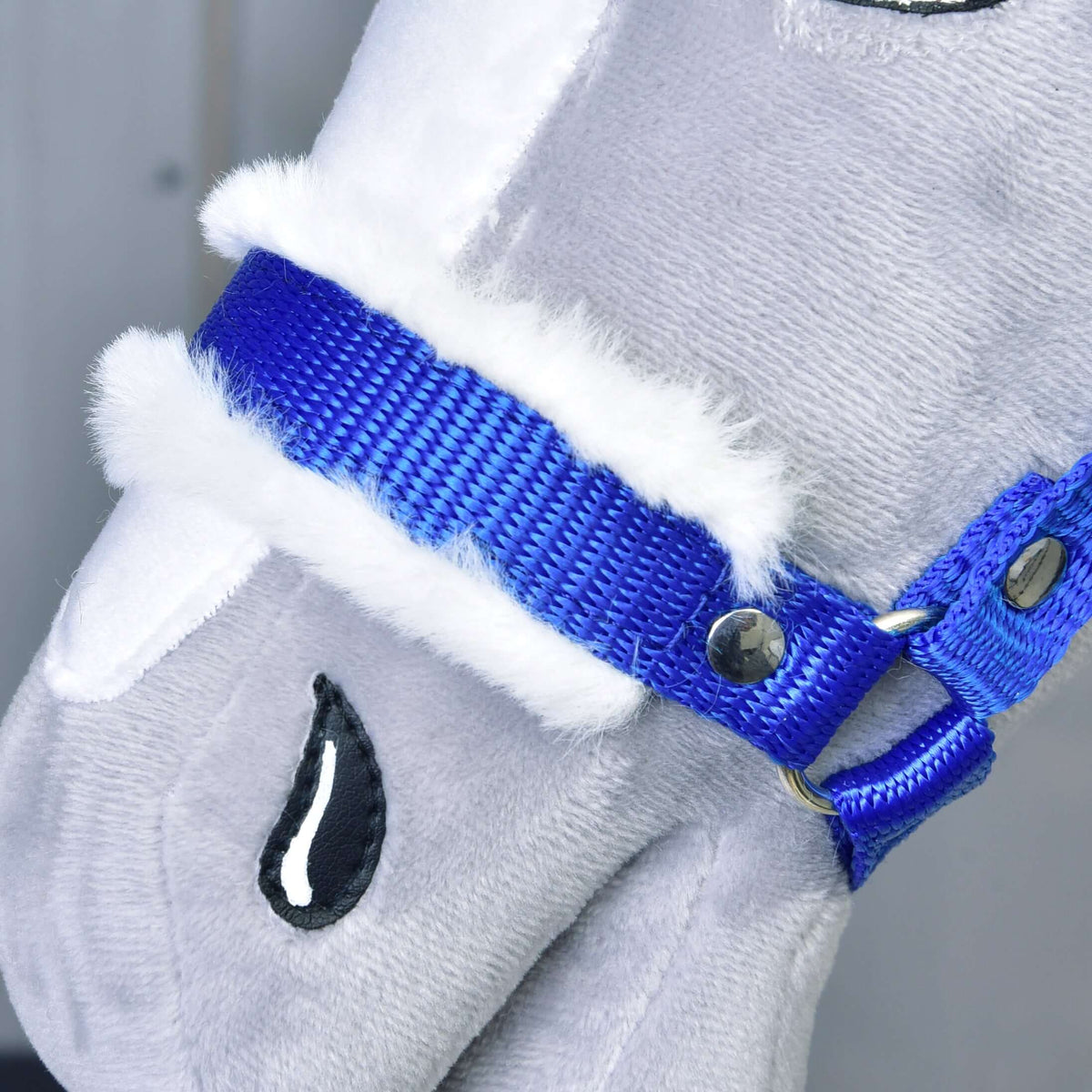 Close-up of the royal blue noseband with soft white fur padding and a silver rivet on a grey plush Hobby Horse