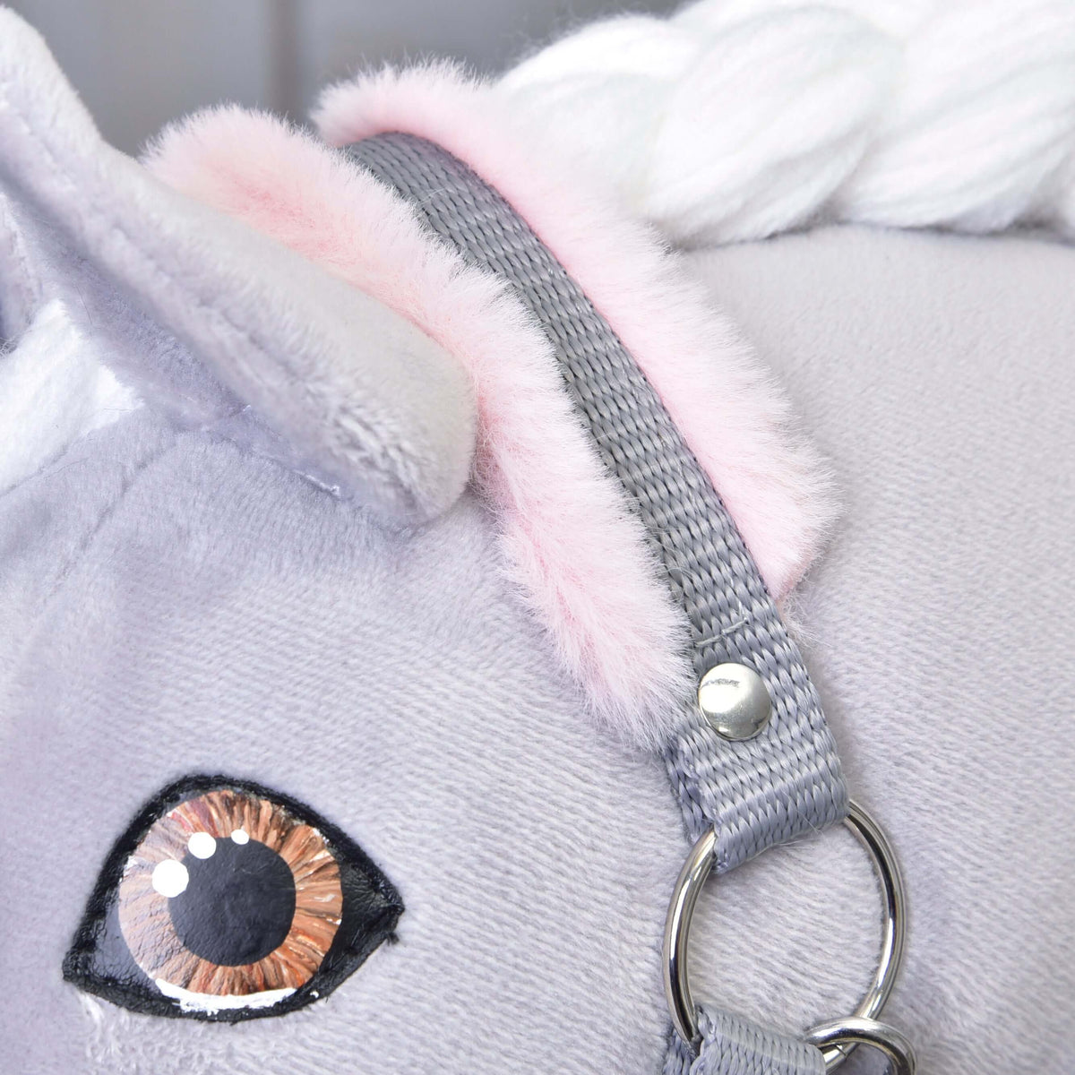Close-up of the grey crownpiece with light pink fur behind the ear and the brown eye of a grey Hobby Horse