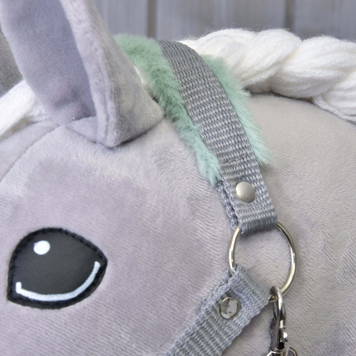 Close-up of the grey crownpiece with mint fur beside the ear and dark eye of a grey plush Hobby Horse