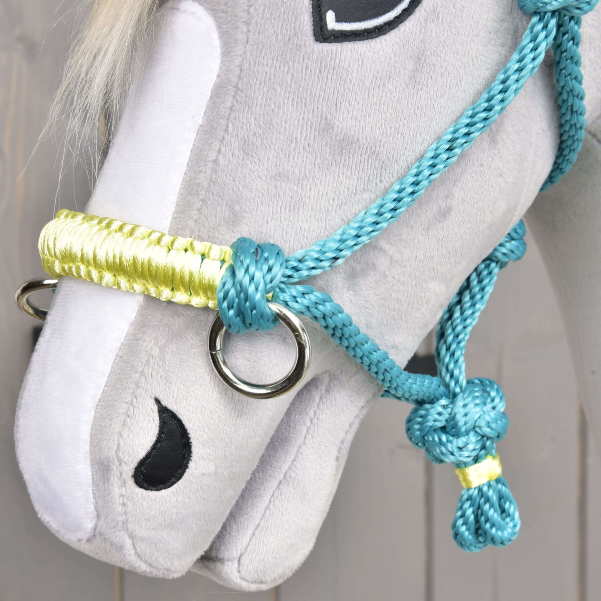 Close-up of the pale yellow braided noseband and silver ring of the turquoise rope halter on a grey plush muzzle