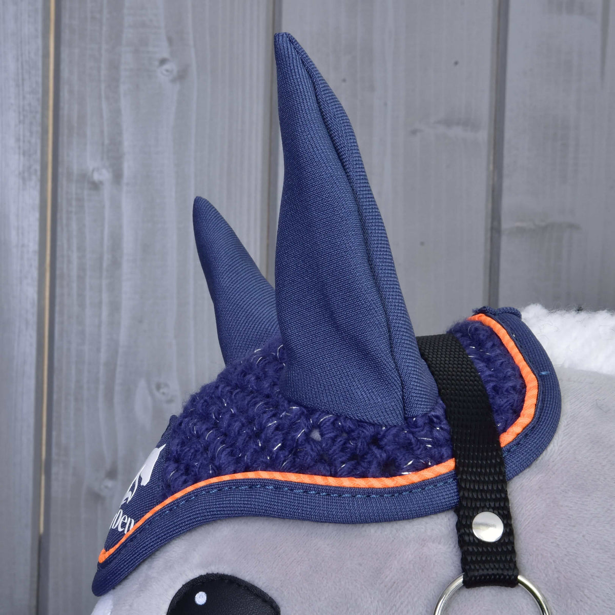 Närbild på de höga marinblå öronen och den orangekantade virkningen på flughuvan Blue Sport bredvid den svarta grimremmen