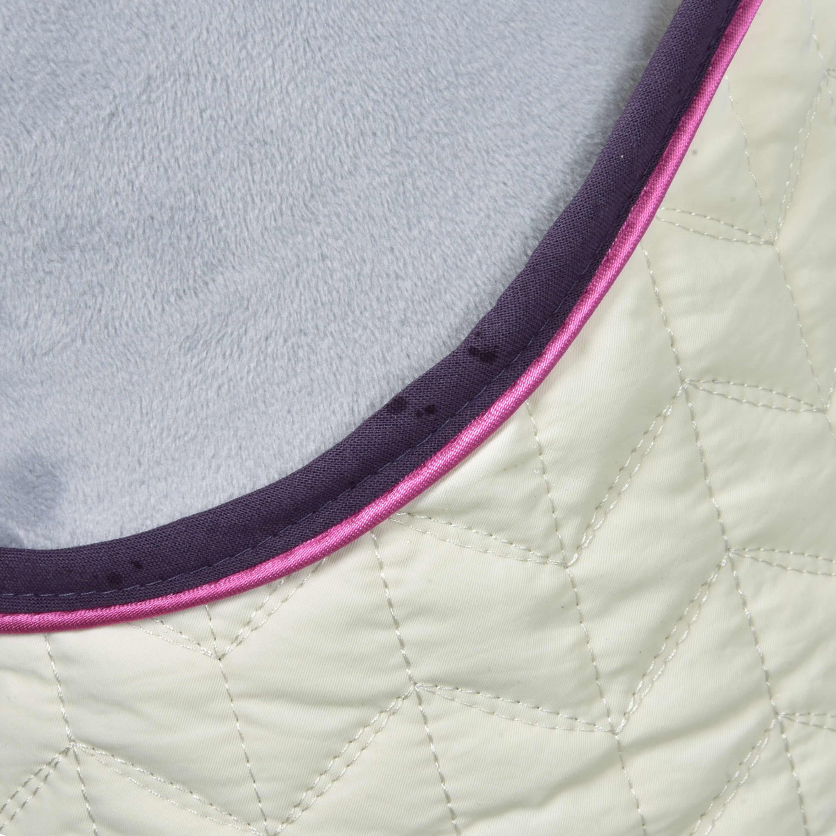 Close-up of the Set Supreme Crema blanket: cream chevron quilting, dark purple binding and pink piping at the neck