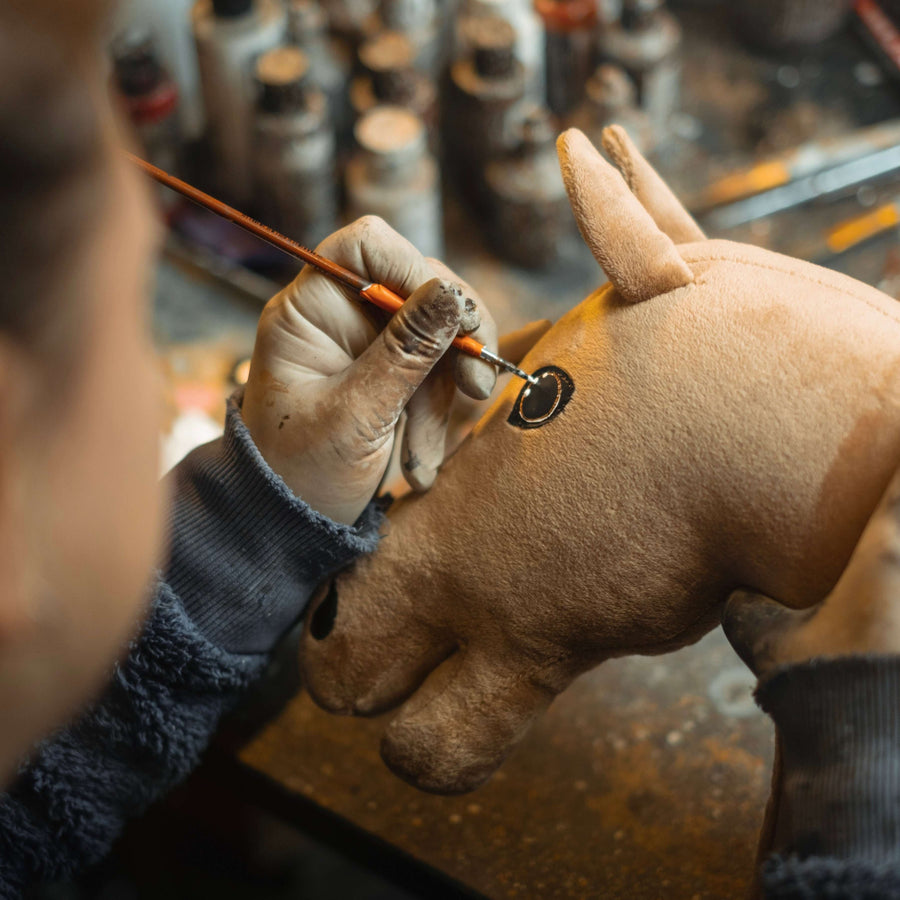 Gloved hand painting the eye of a light brown Hobby Horse head with a fine brush in a workshop