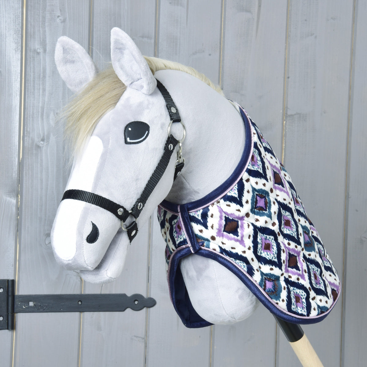 Grey Hobby Horse with a cream mane and black halter wearing the Indian blanket, seen from the front at a grey wooden door