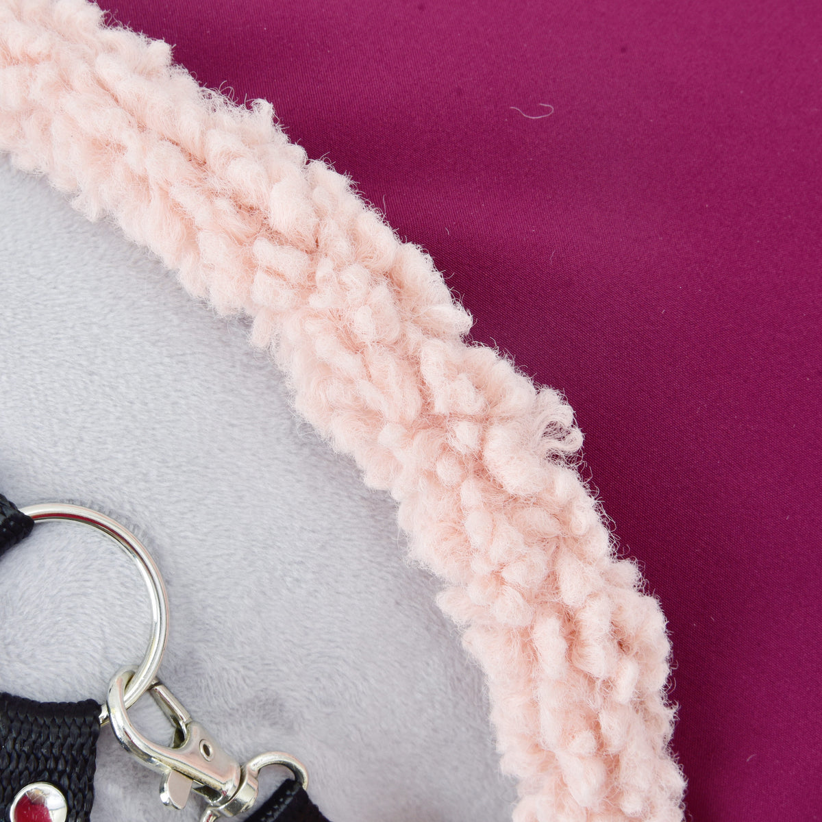 Close-up of the pale pink curly fleece edge on the burgundy fabric of the Stable Blanket Royal Burgundy on a grey Hobby Horse