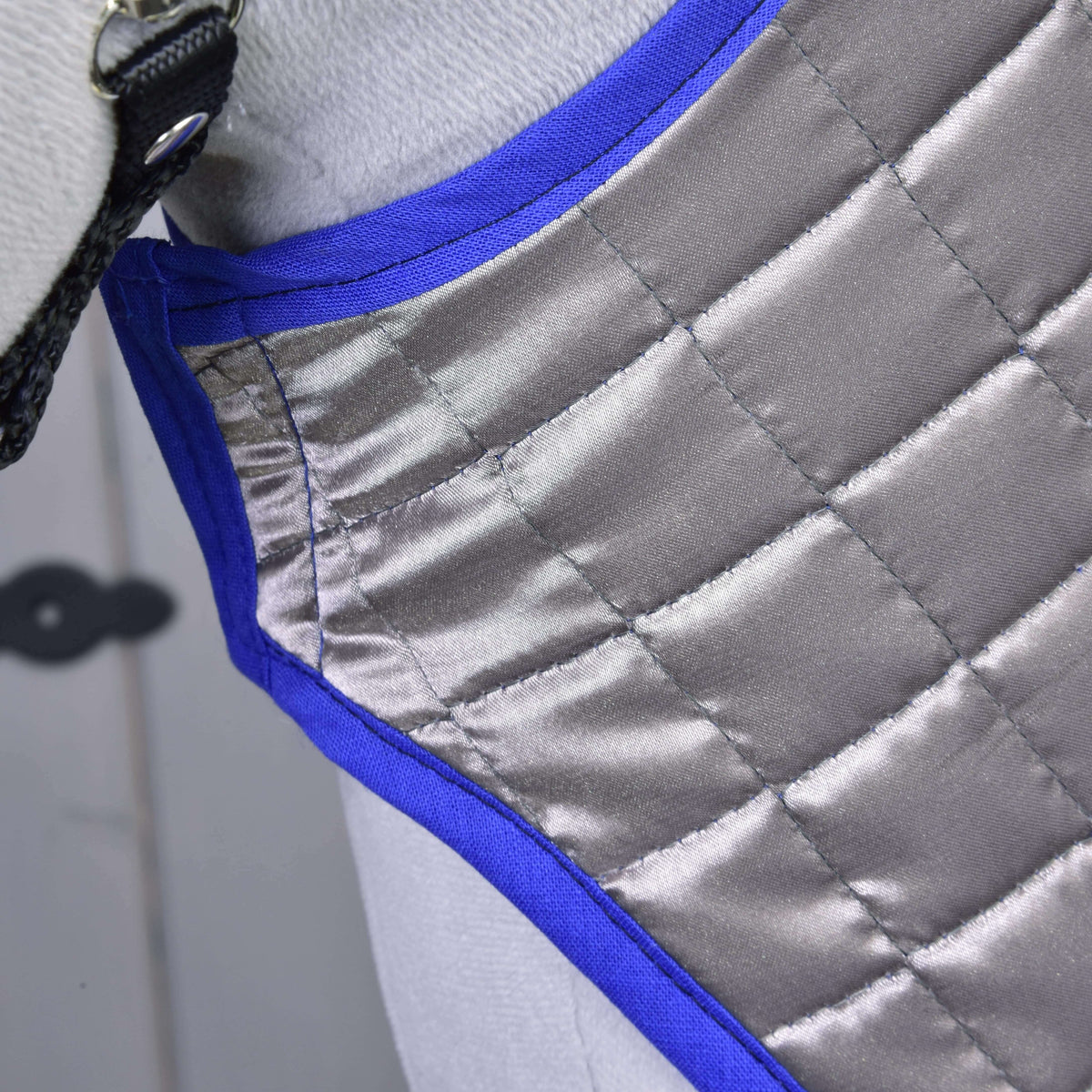 Close-up of the silver-grey quilted side of the reversible Blanket DeLuxe Blue on a grey Hobby Horse, edged in royal blue
