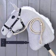 Cream and beige braided lead rope clipped to the black halter of a grey Hobby Horse by a grey wooden wall