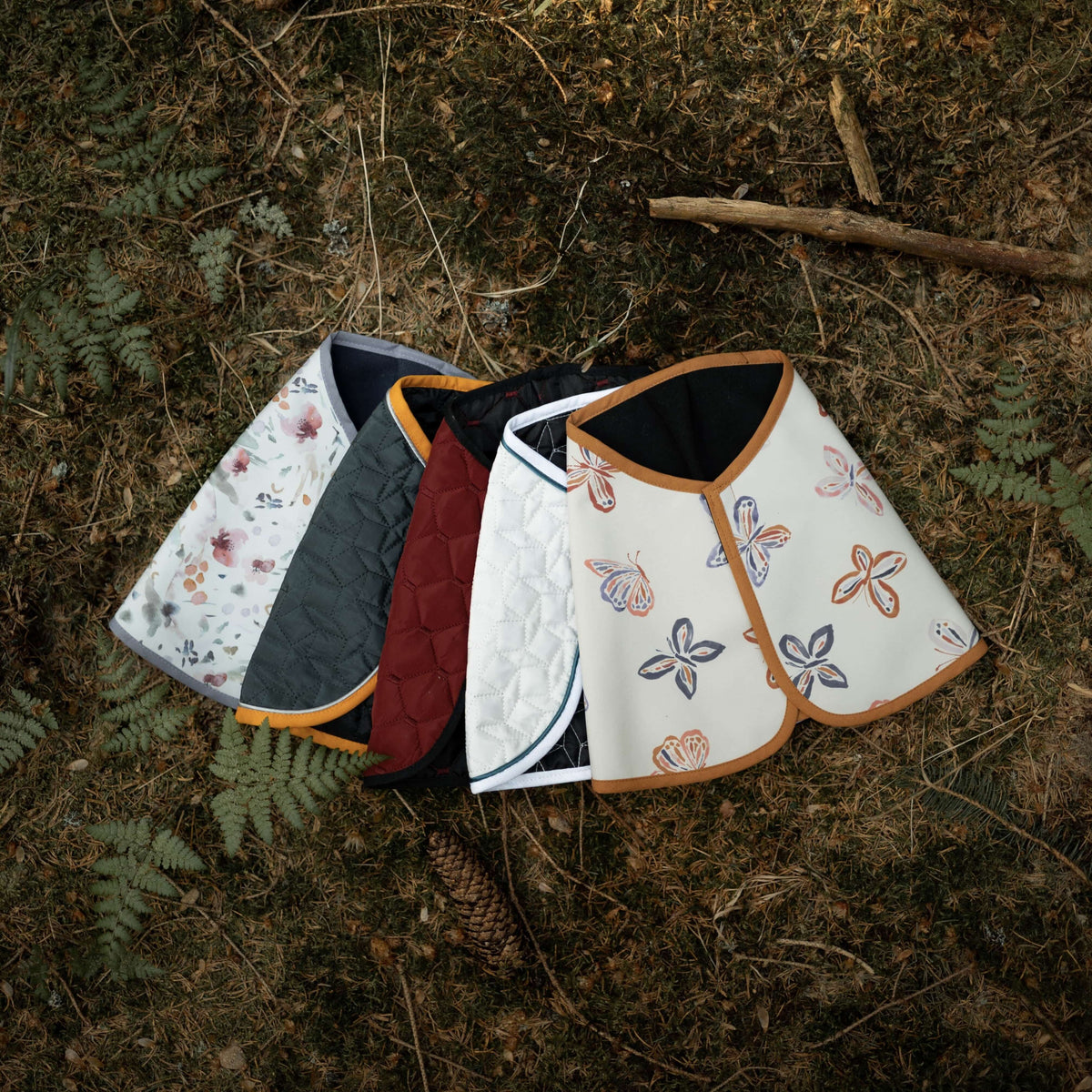 Five Hobby Horse blankets fanned out on the forest floor: floral, dark green, burgundy, white quilted and butterfly print