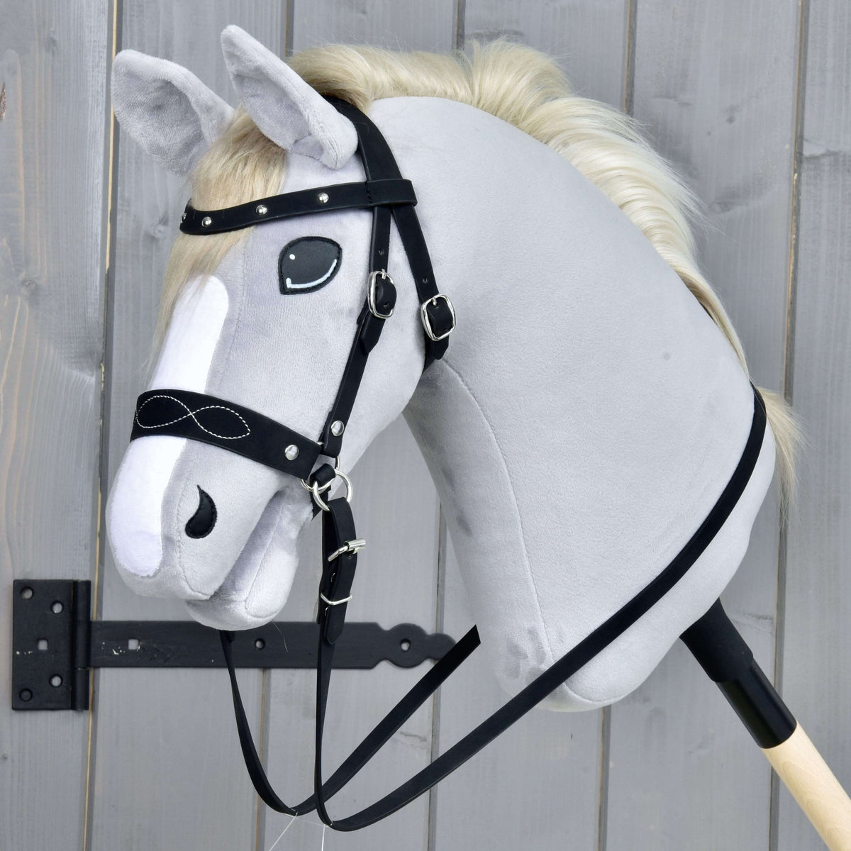 Hobby Horse komplett bettlöst träns, dekorerat, från LarDen på ett grått käpphästhuvud i plysch: nosgrimma med vita sömmar, pannband med nitar