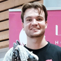 Smiling LarDen maker with a dark grey Hobby Horse with a grey yarn mane in front of a pink banner