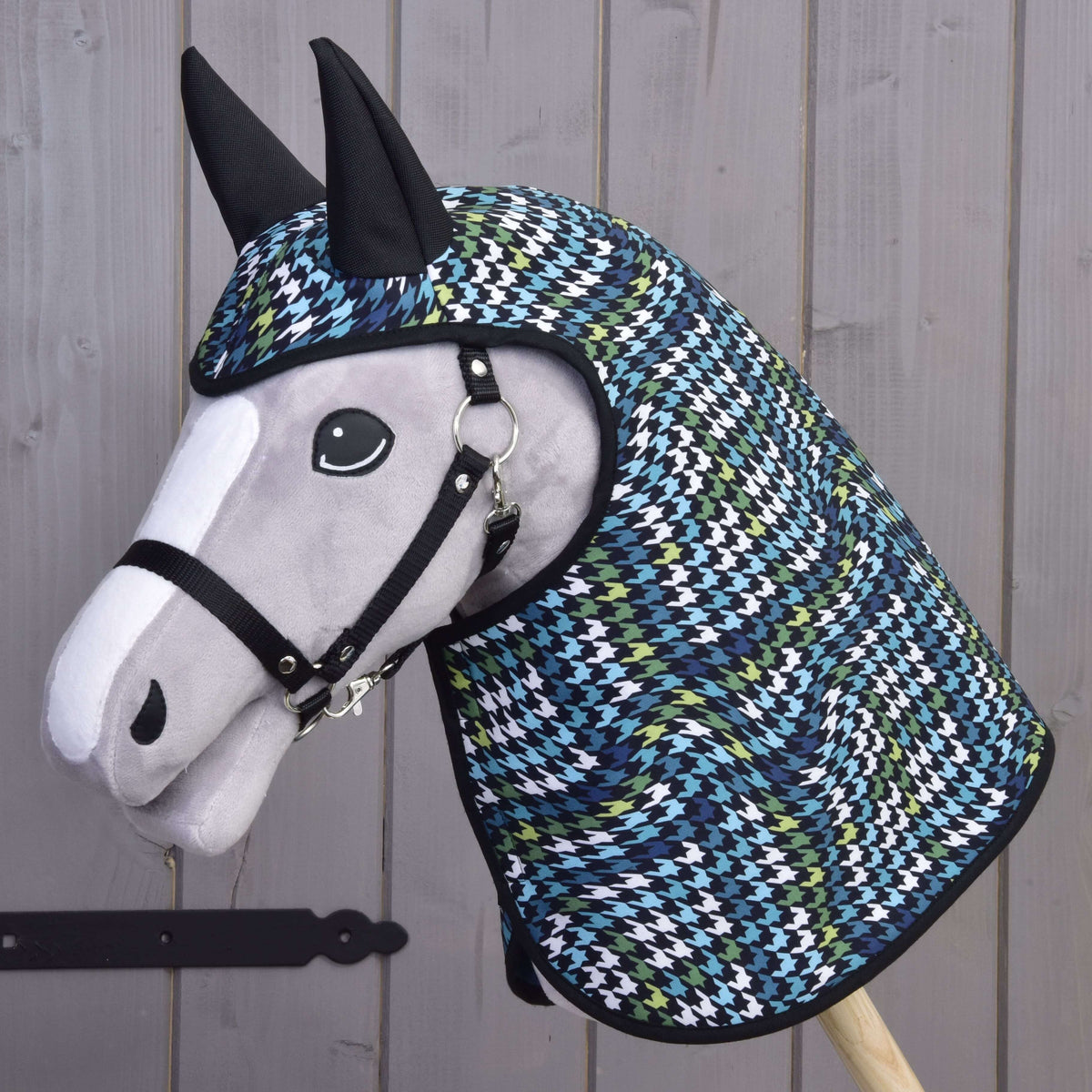 Grey Hobby Horse with a black halter wearing the Raincoat Lara, its houndstooth hood with black ears covering the head