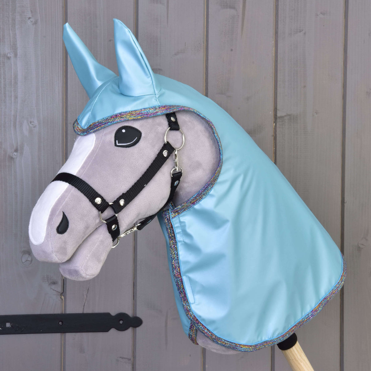 Grey Hobby Horse with black halter wearing the glossy Raincoat Light Blue with ears and rainbow glitter edging